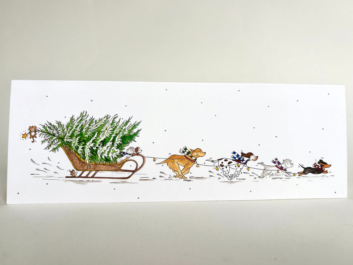 Fun dog charity Christmas card featuring an original watercolour illustration of dogs pulling a Christmas tree through the snow on a sleigh