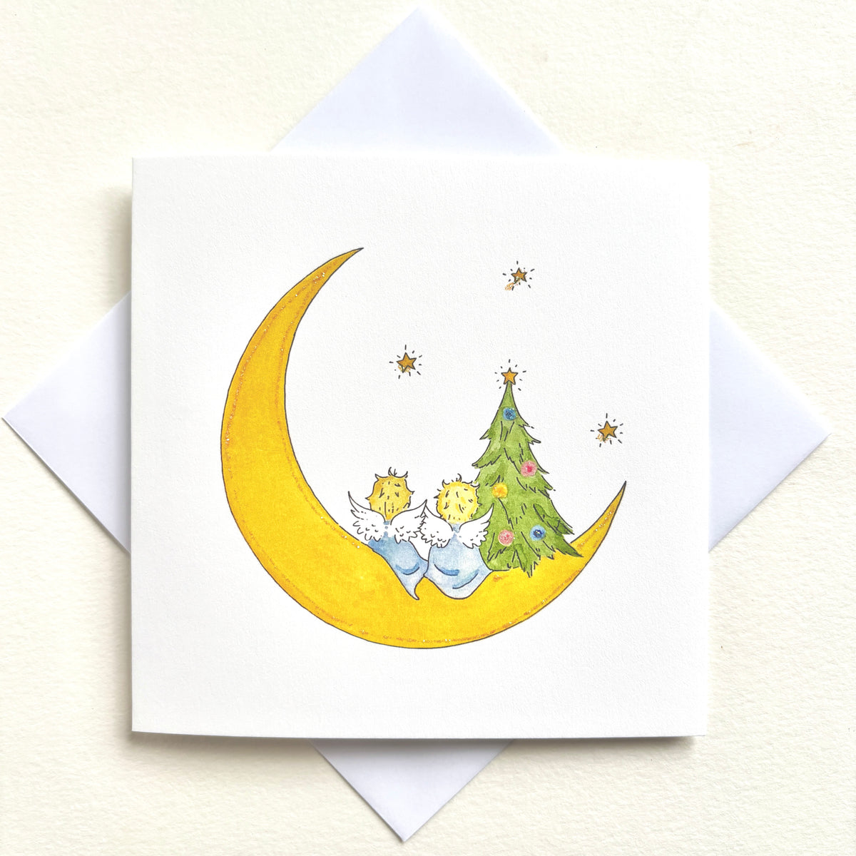 Two little angels perched on a crescent moon beside a decorate Christmas tree looking out at tiny stars. Hand finished with or without glitter. Own Christmas watercolour illustration 