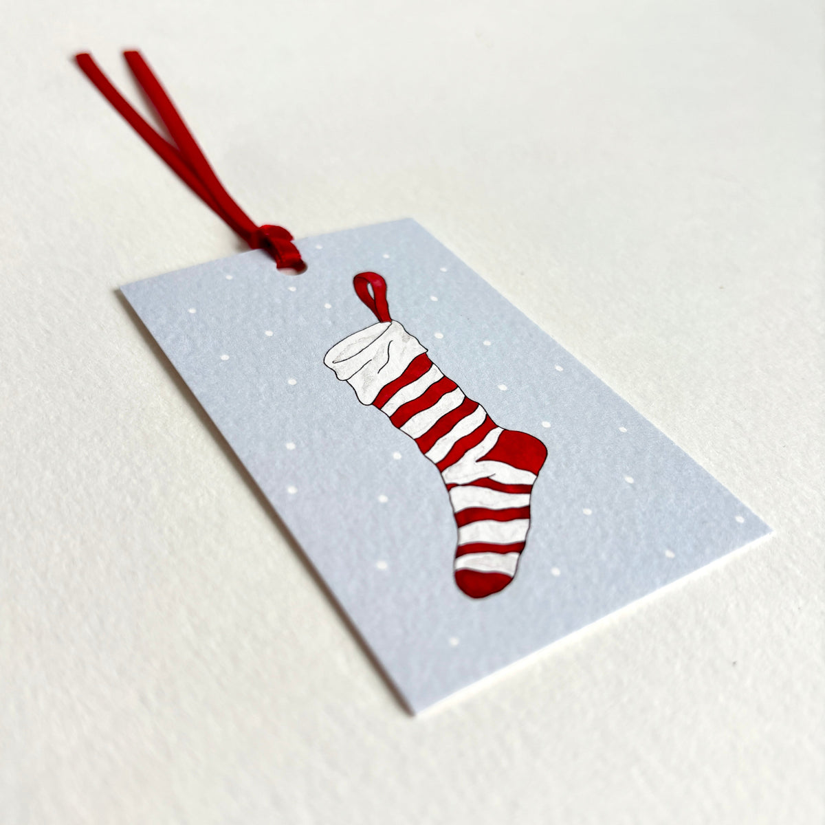 Angle image showing luxury textured cardstock for rectangular Christmas Stocking gift tag with a hand-tied red ribbon.