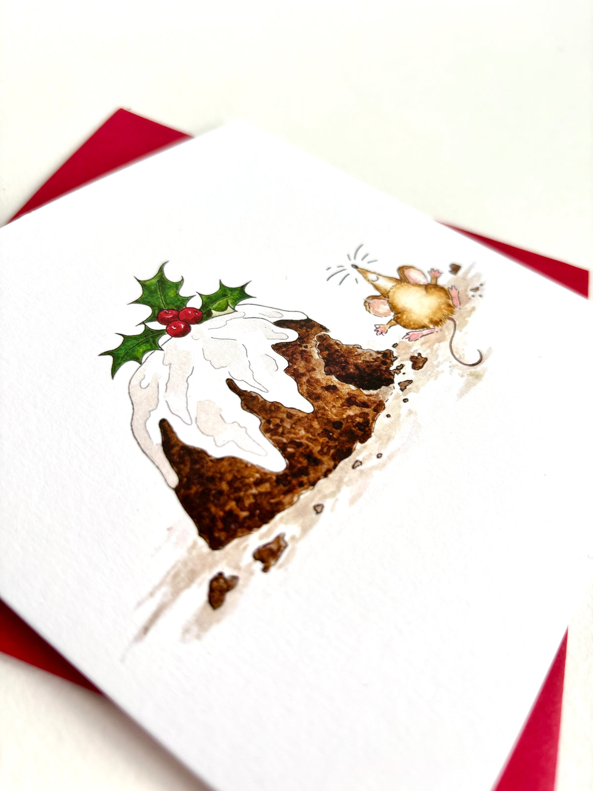 Detail of hand-painted illustration of a mouse beside a Christmas pudding with dripping white icing, a green holly sprig with red berries. Printed in the UK using fine quality, 300gsm soft white matt cardstock (FSC certified)