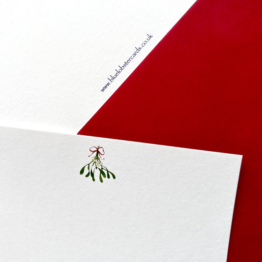 A close-up of a single white textured card mistletoe watercolour illustration, layered over a red envelope. The card shows the Blue Lobster Cards website www in svery small printed as appears on each card's reverse, set against a coordinated Christmas red envelope. Part of of pack of 6 or 10 mistletoe cards