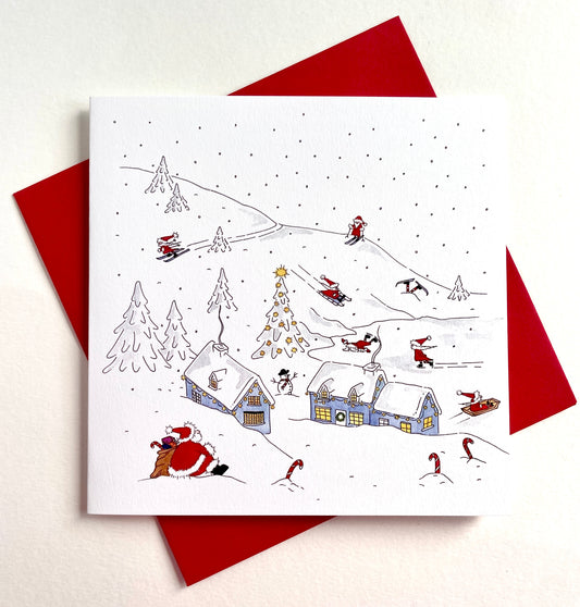 A square white greeting card showing a hand-drawn winter holiday snow scene, with Santa Claus, wtaching his helpers hae fun amidst snow-covered houses, trees, and sledders. Packs and single cards are supplied with red envelopes.
