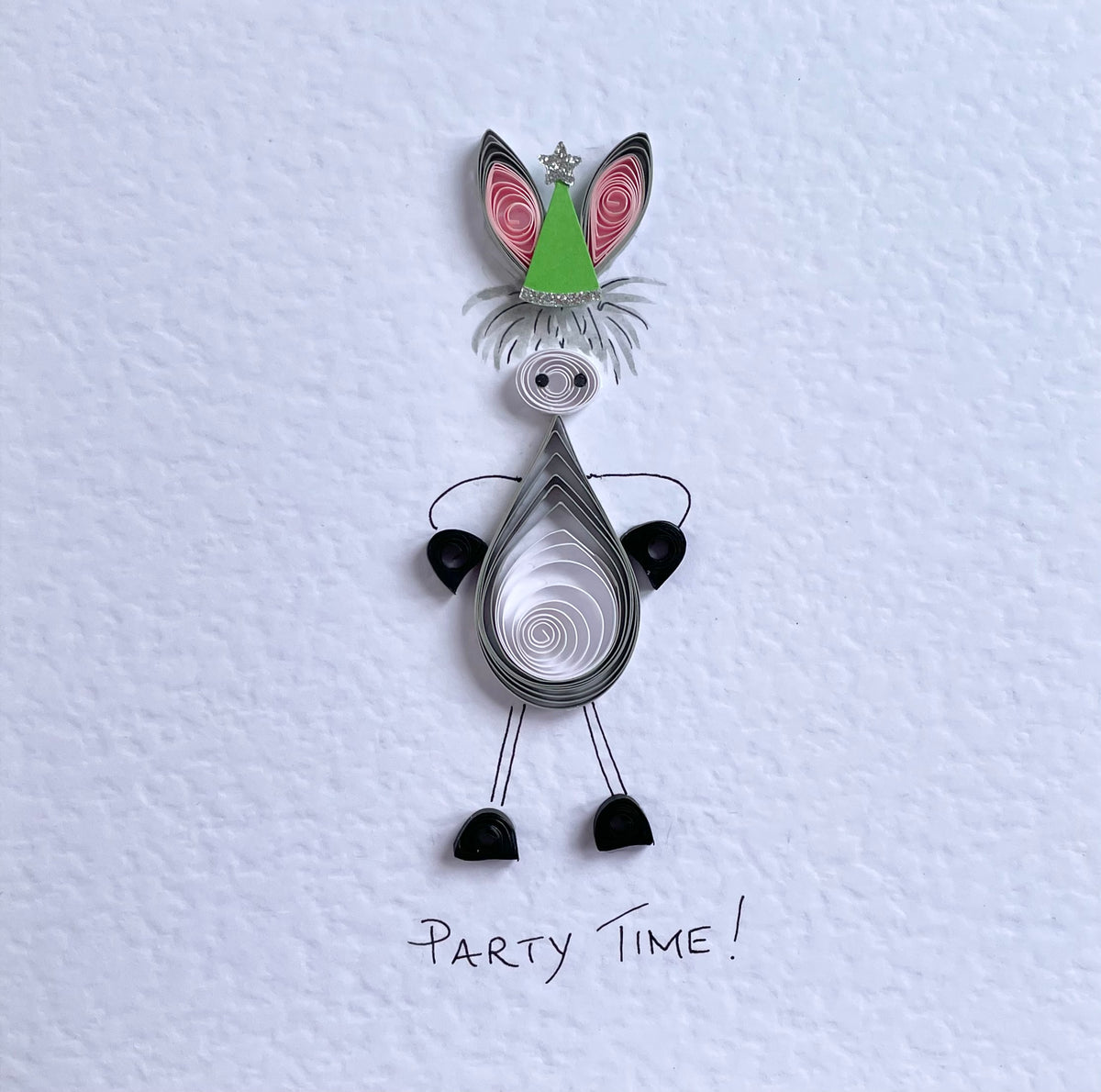 Detail of quilled donkey card with Green Party hat trimmed with glitter star. Displayed on lovely quality white hammered cardstock