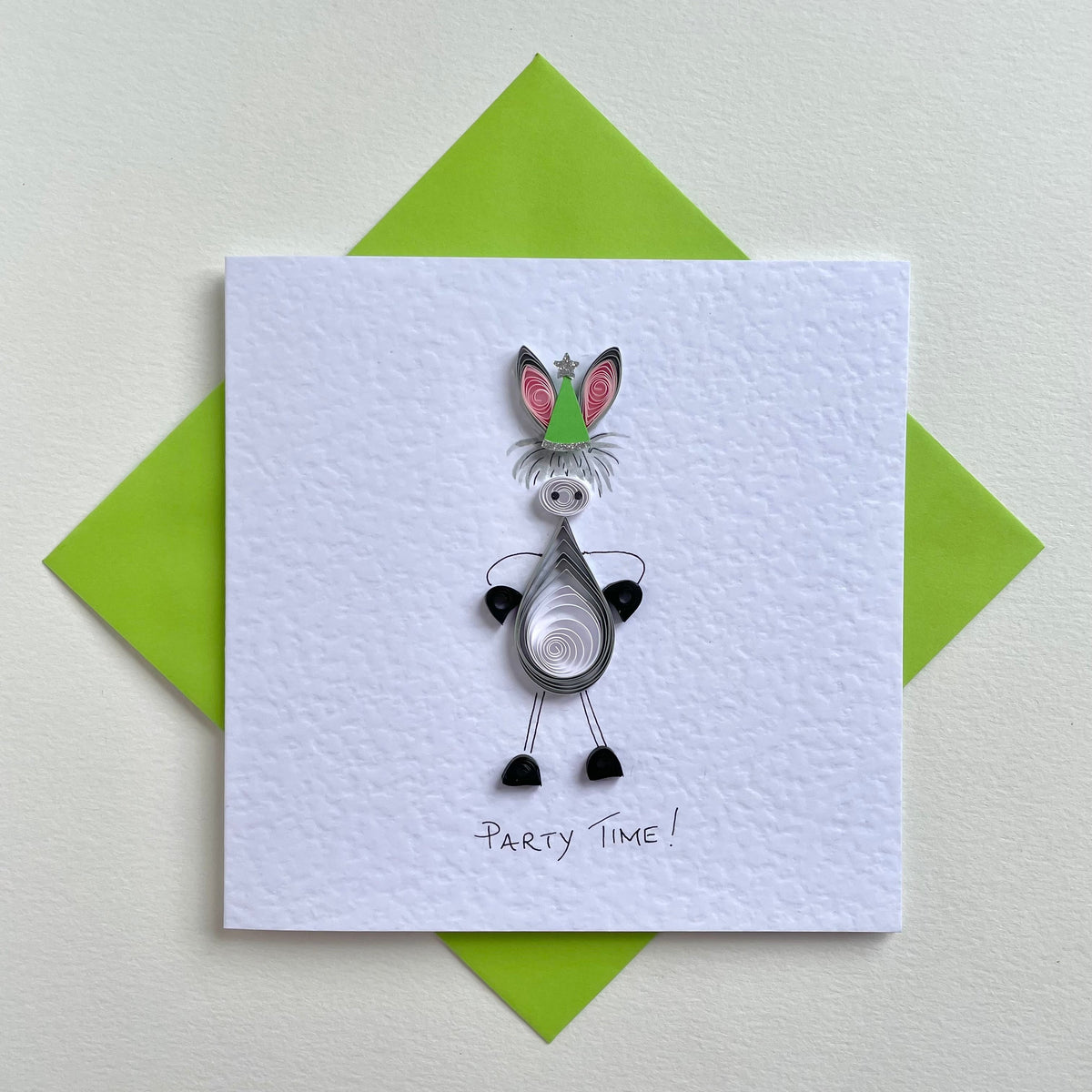 A handmade greeting card featuring a quilled paper donkey with green party hat, and the text 'Party Time' written at the bottom. The card is accompanied by a green envelope.