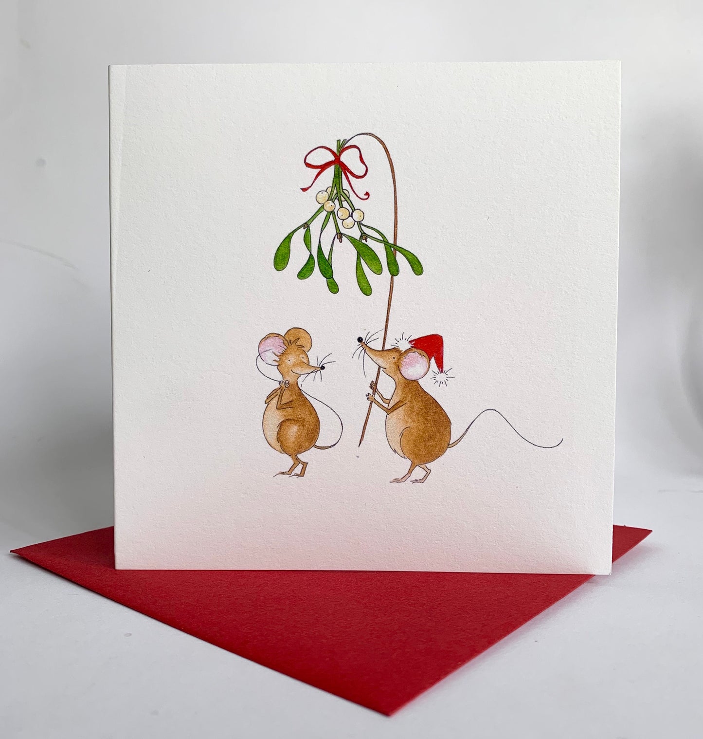 Cute watercolour illustration of two mice benath a branch of misteltoe tied with christmas ribbon