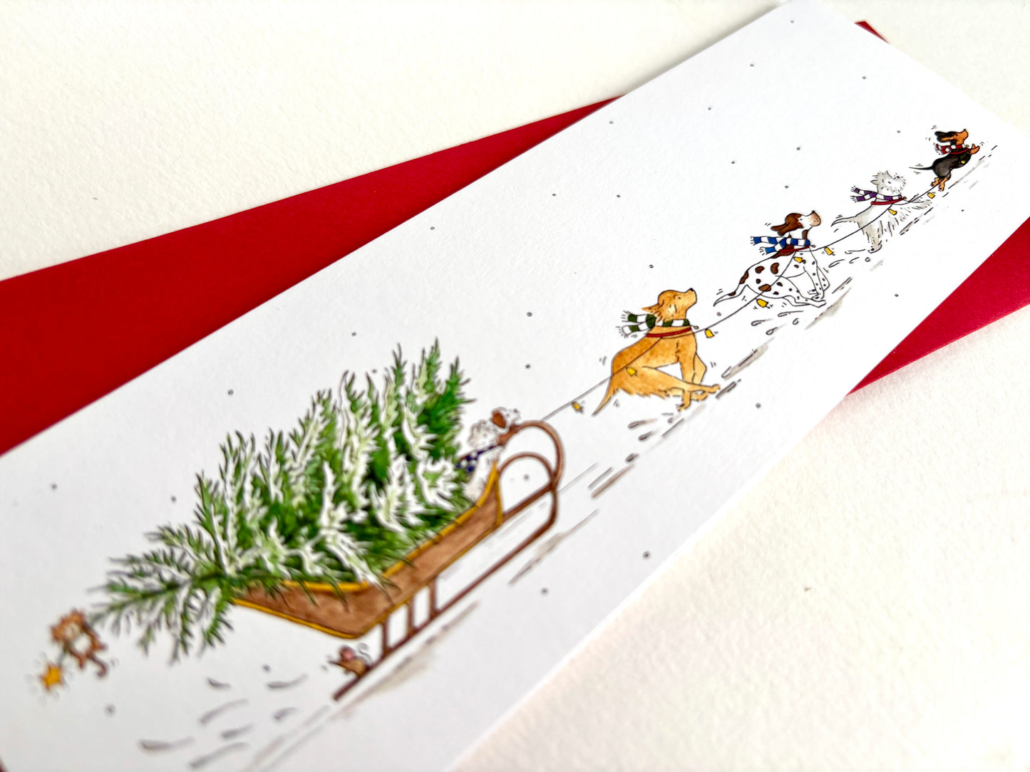 Close-up of the original watercolour Dog Sleigh Christmas card, with festive dogs racing through the snow and pulling a snowy Christmas tree on sleigh