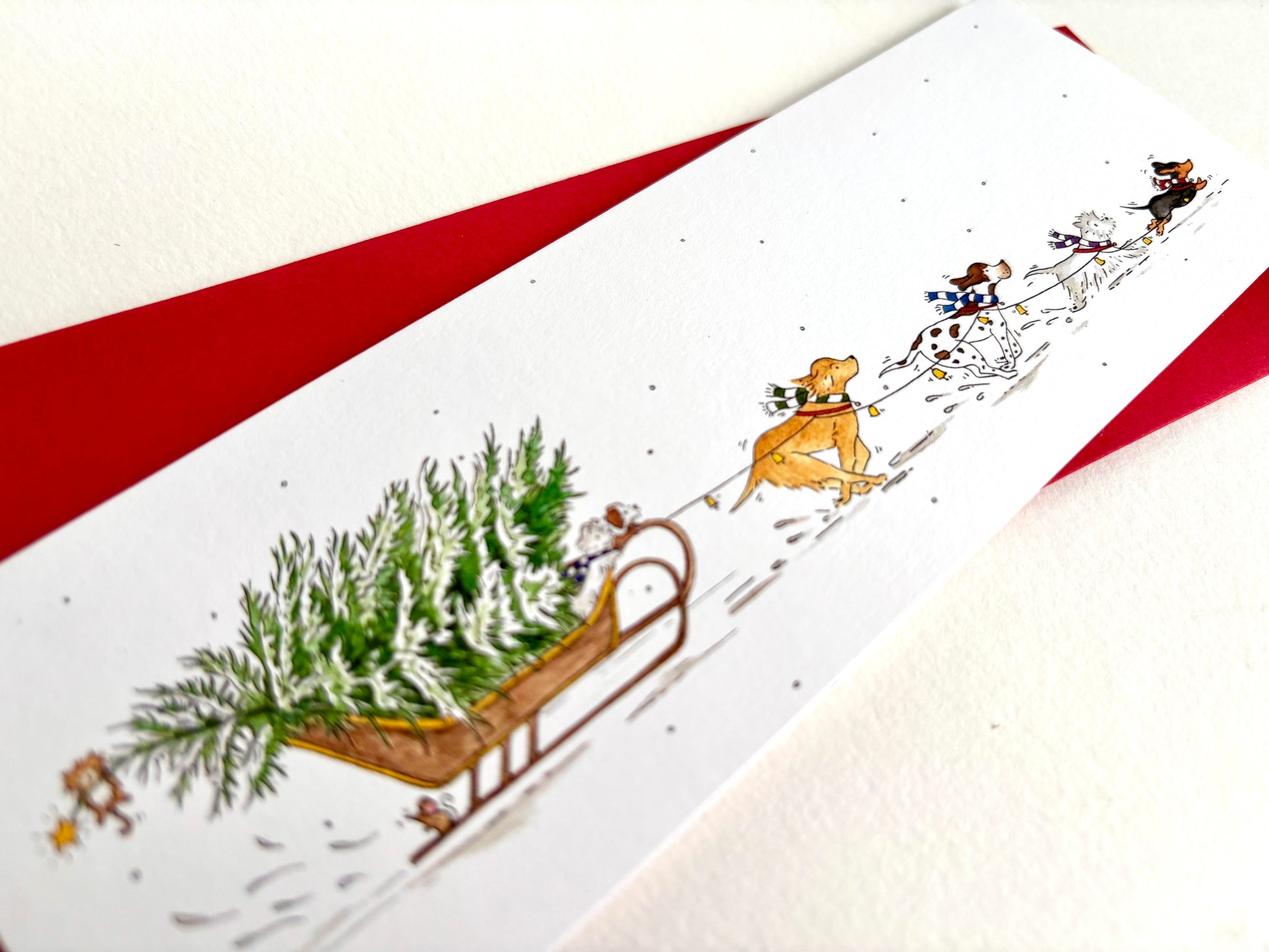 Close-up of the original watercolour Dog Sleigh Christmas card, with festive dogs racing through the snow and pulling a snowy Christmas tree on sleigh