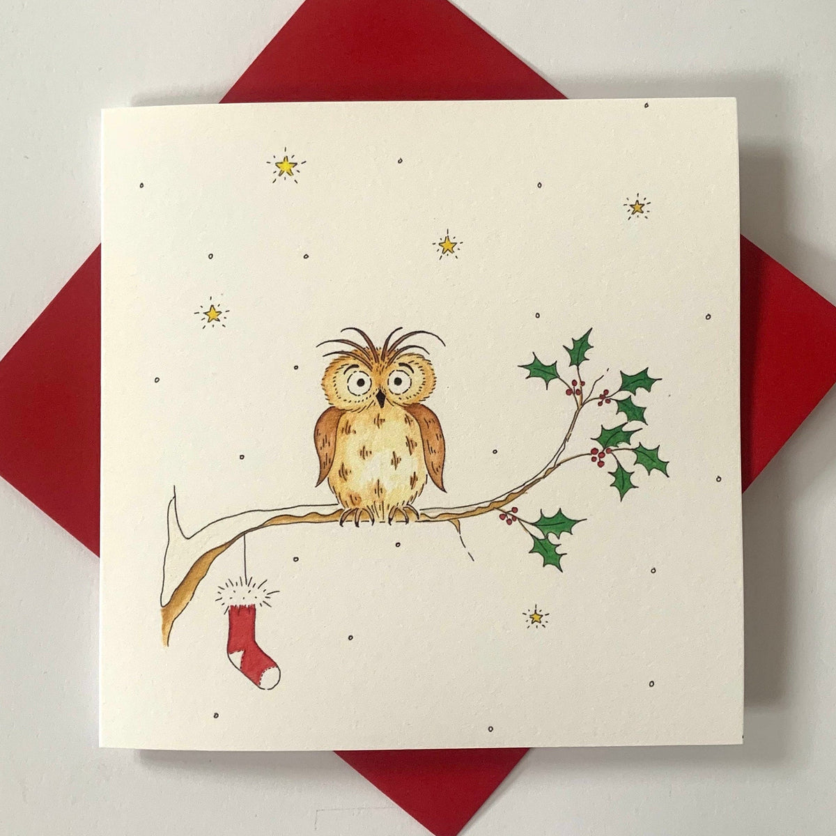 A traditional Christmas card featuring a snowy night scene with an owl hanging its stocking from a holly branch.
