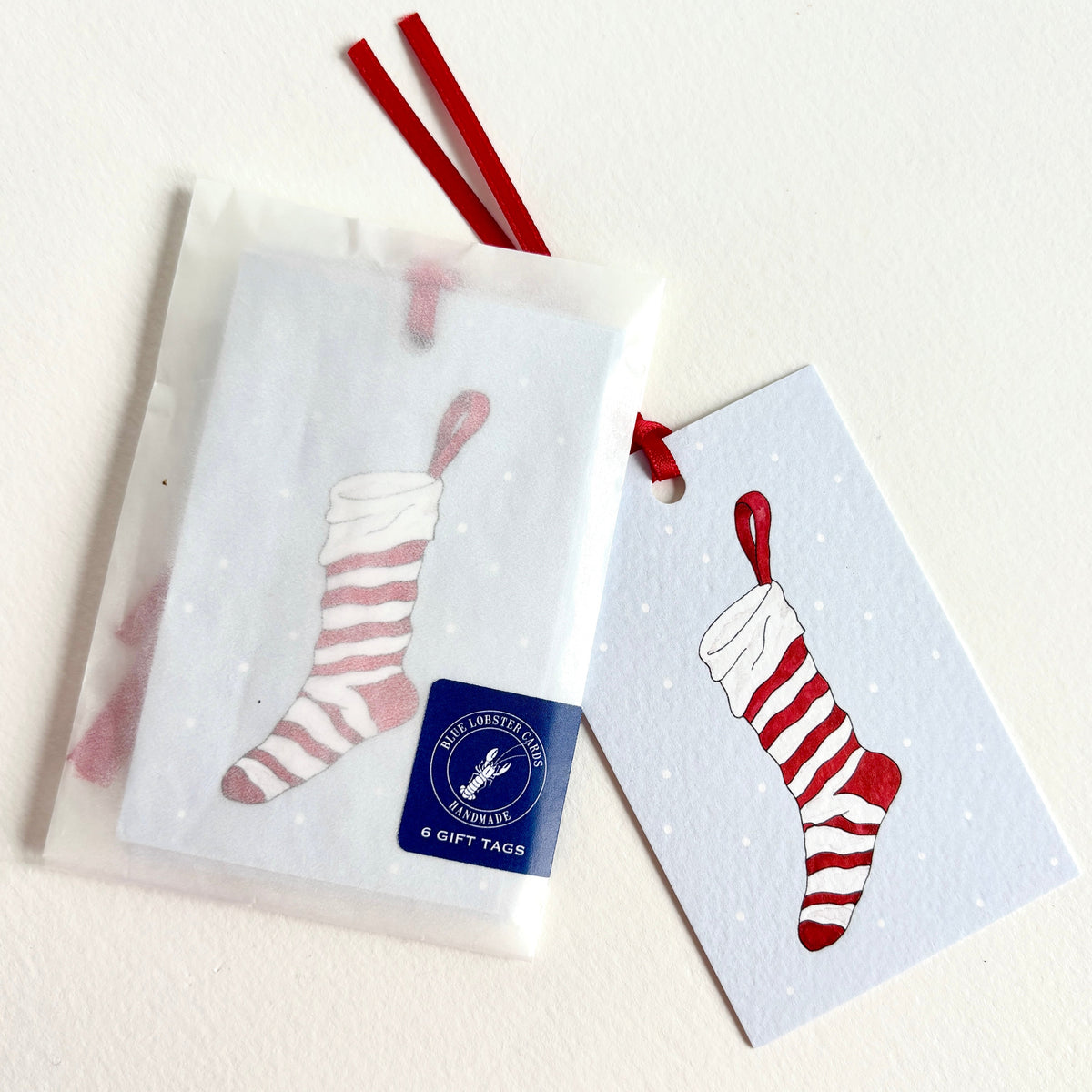 6 tags per pack printed in the UK onto sustainably sourced 300gsm cardstock. Hand finished with red satin ribbon and sealed in a recyclable glassine sleeve with Blue Lobster Cards branding