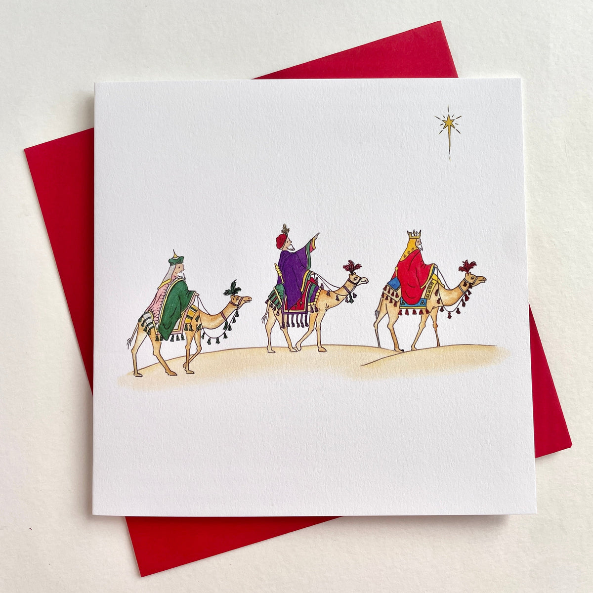 Close-up view to chow watercolour artwork and fine quality softly textured FSC cardstock, set against coordinating red envelope - nativity scene featuring Three Wise Men on camels