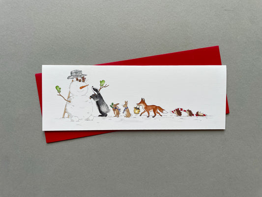 Woodland animals building a snowman on a Christmas card, photographed from above with a red envelope
