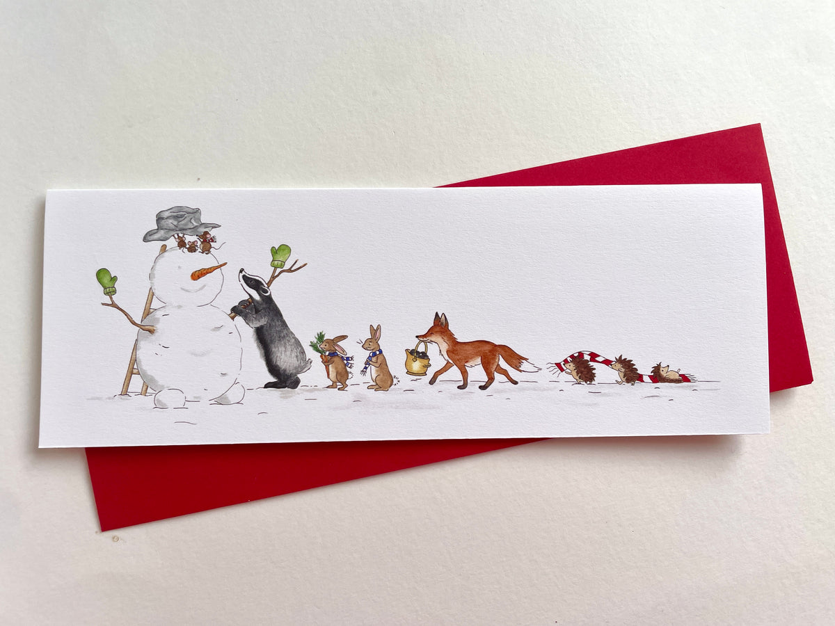 Woodland animals snowman Christmas card resting on a red envelope against a white background