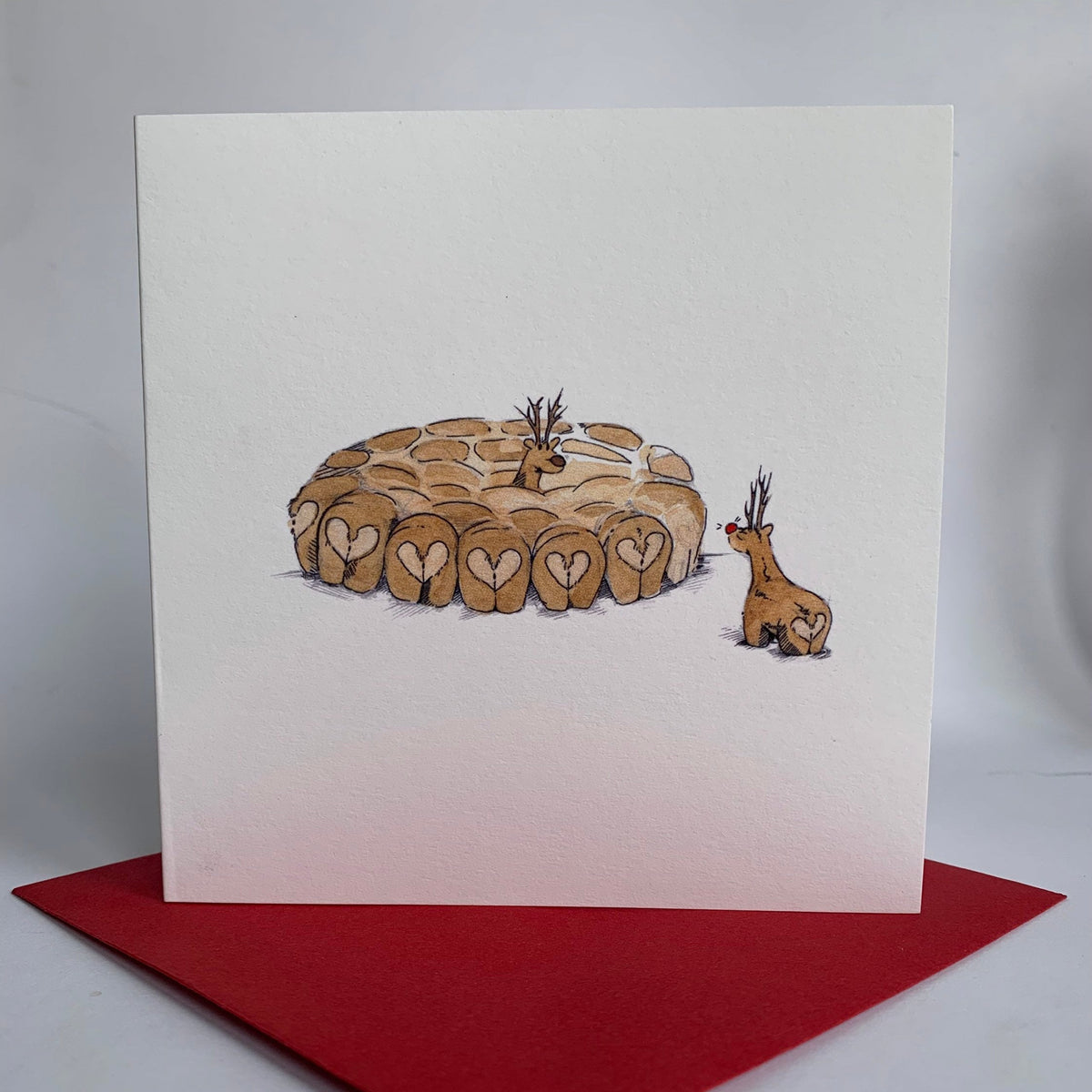 Square charity christmas card featuring two reindeer (with heart shaped bottoms) locking eyes in a snow storm 