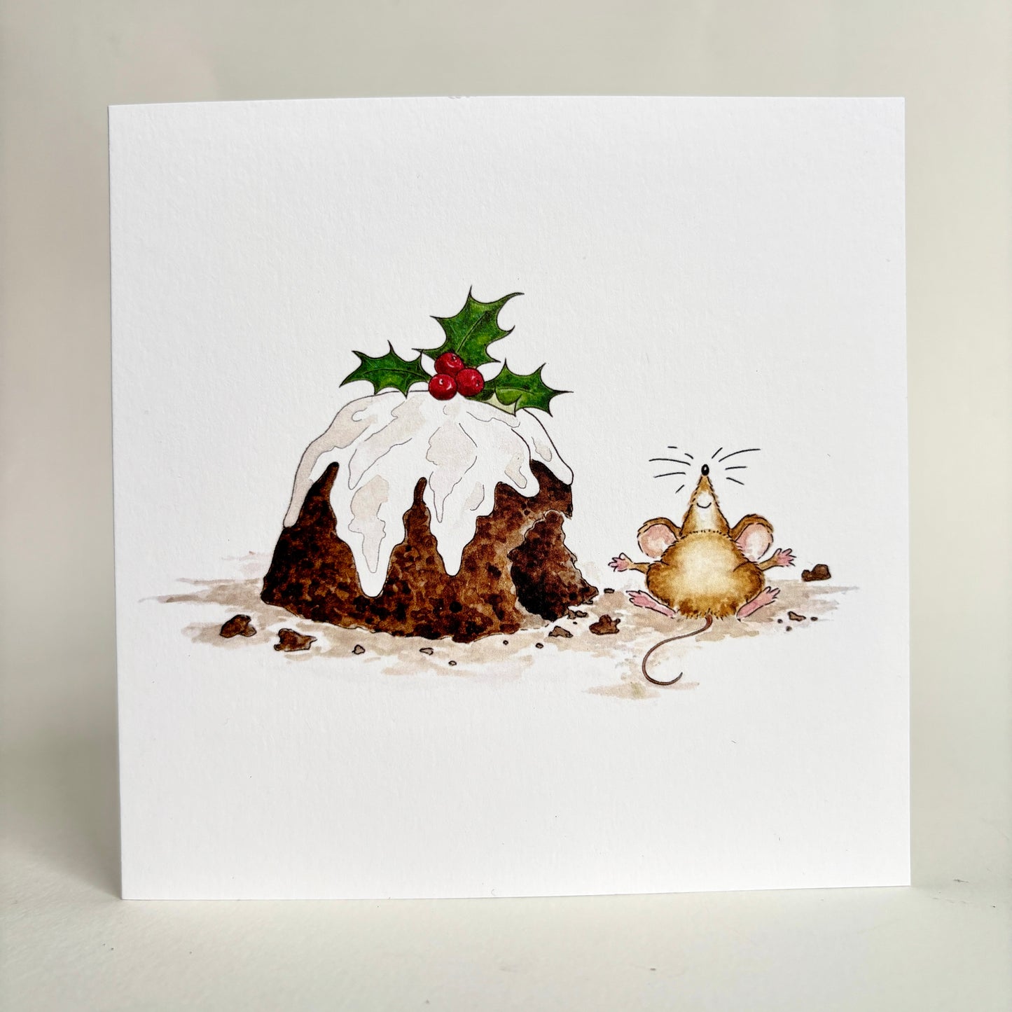 Standing image of square Christmas card card featuring a watercolour illustration of a mouse beside a partially nibbled Christmas pudding