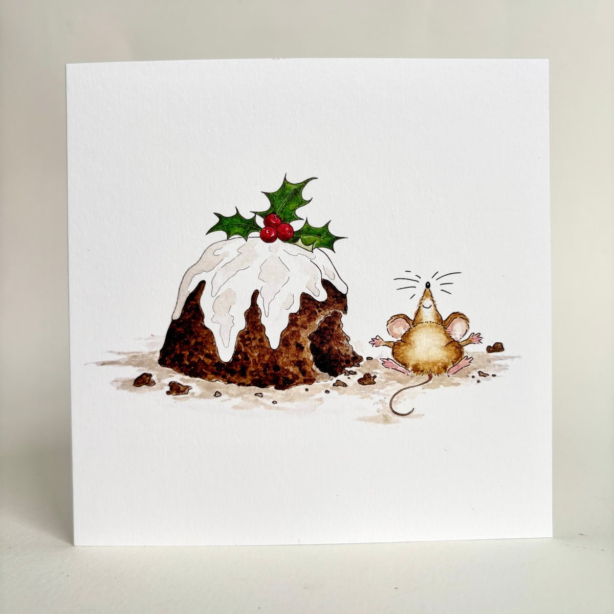 Standing image of square Christmas card card featuring a watercolour illustration of a mouse beside a partially nibbled Christmas pudding