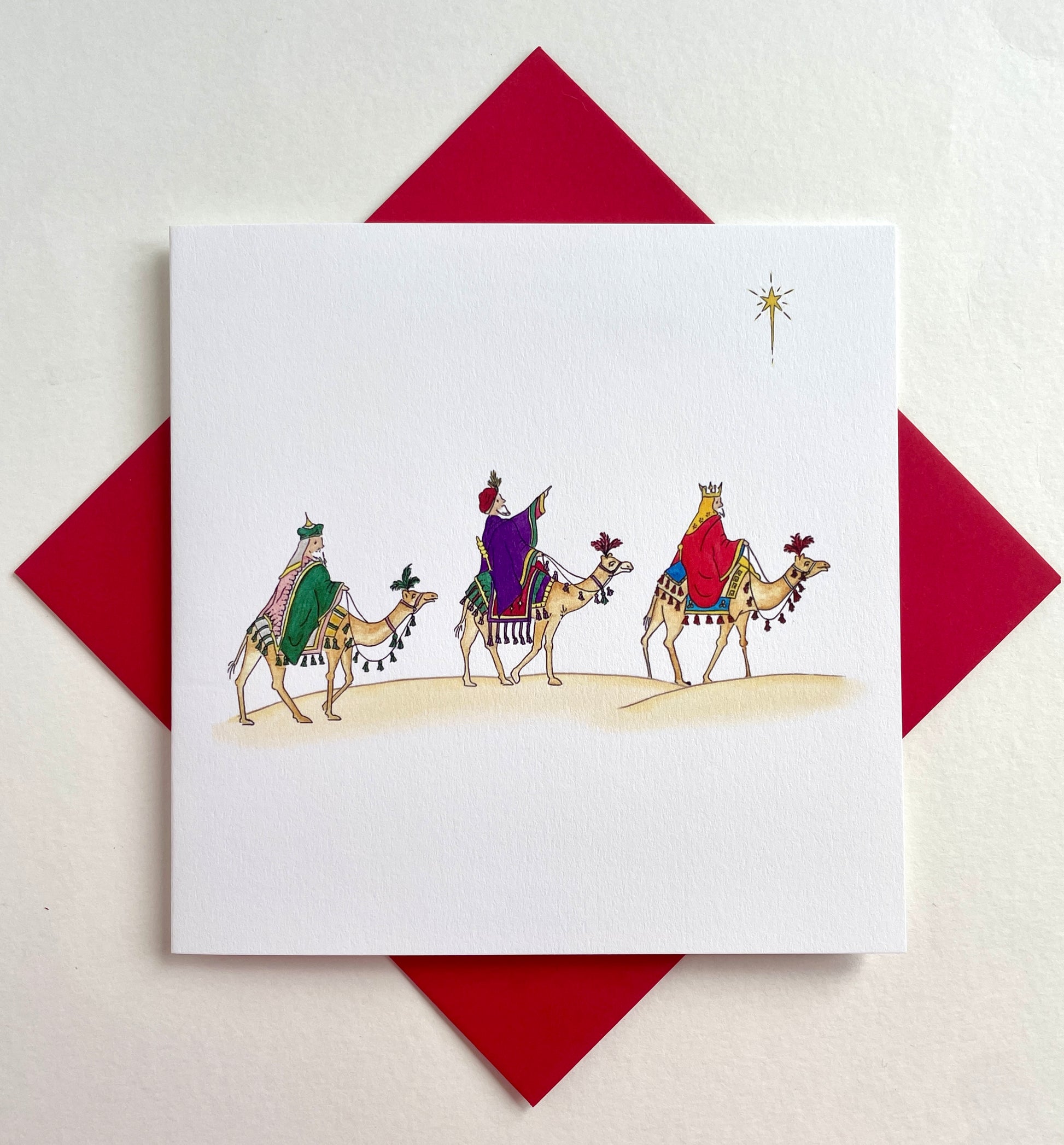 Square Christmas card with watercolour illustration of three wise men on camels with coordinating red envelope beneath