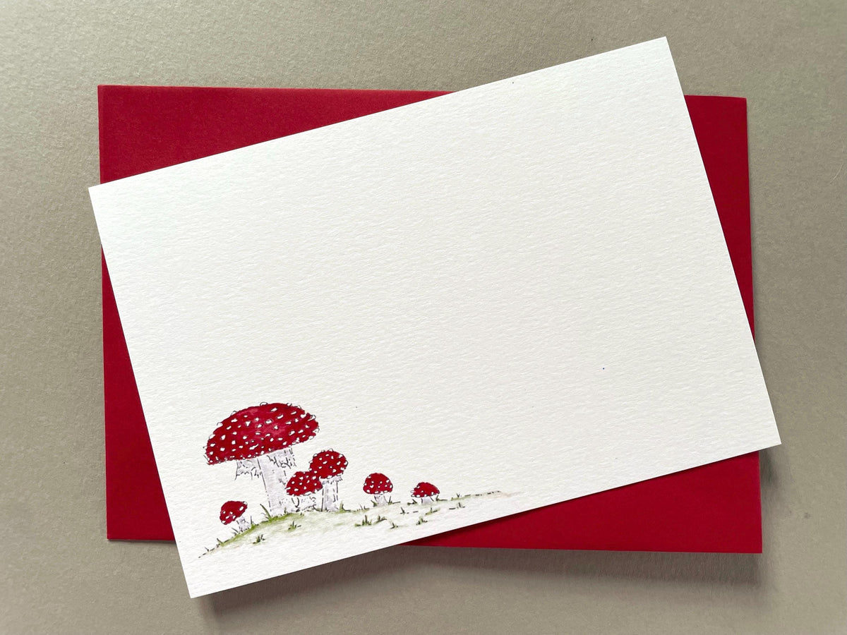 Fungi watercolour notecard with a red envelope, featuring an illustration of red and white spotted fly agaric toadstools on a white background. The envelope is shown with the notecard