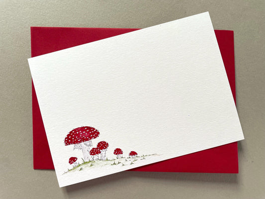 Fungi watercolour notecard with a red envelope, featuring an illustration of red and white spotted fly agaric toadstools on a white background. The envelope is shown with the notecard