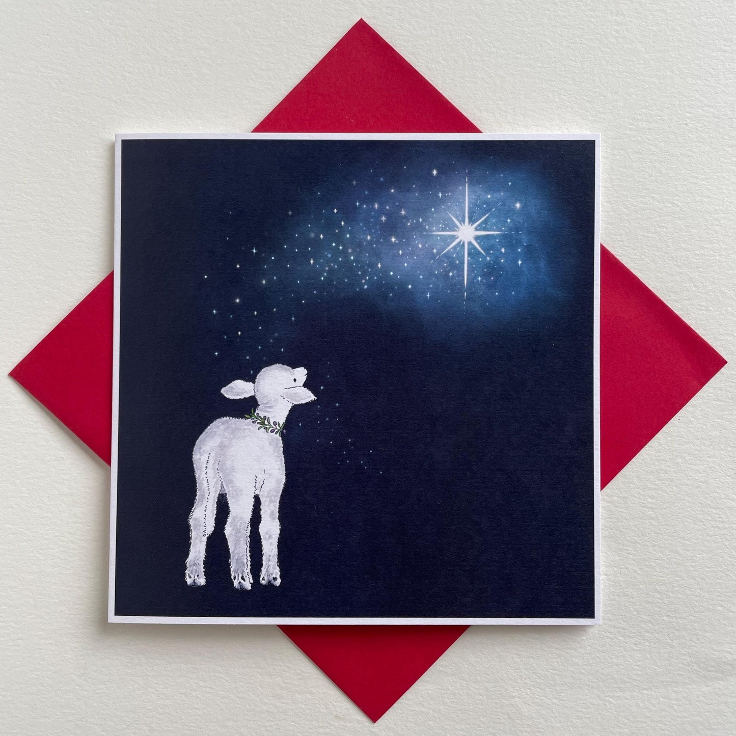 A peaceful Christmas card featuring a traditonal nativity scene with a lamb and a starry night sky in the background, presented on a red envelope.