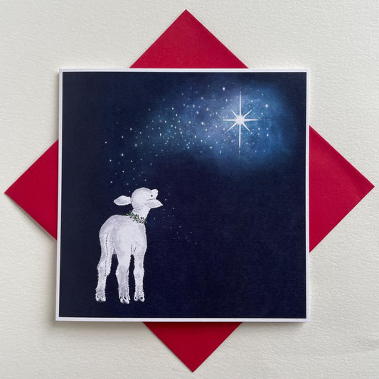 A peaceful Christmas card featuring a traditonal nativity scene with a lamb and a starry night sky in the background, presented on a red envelope.