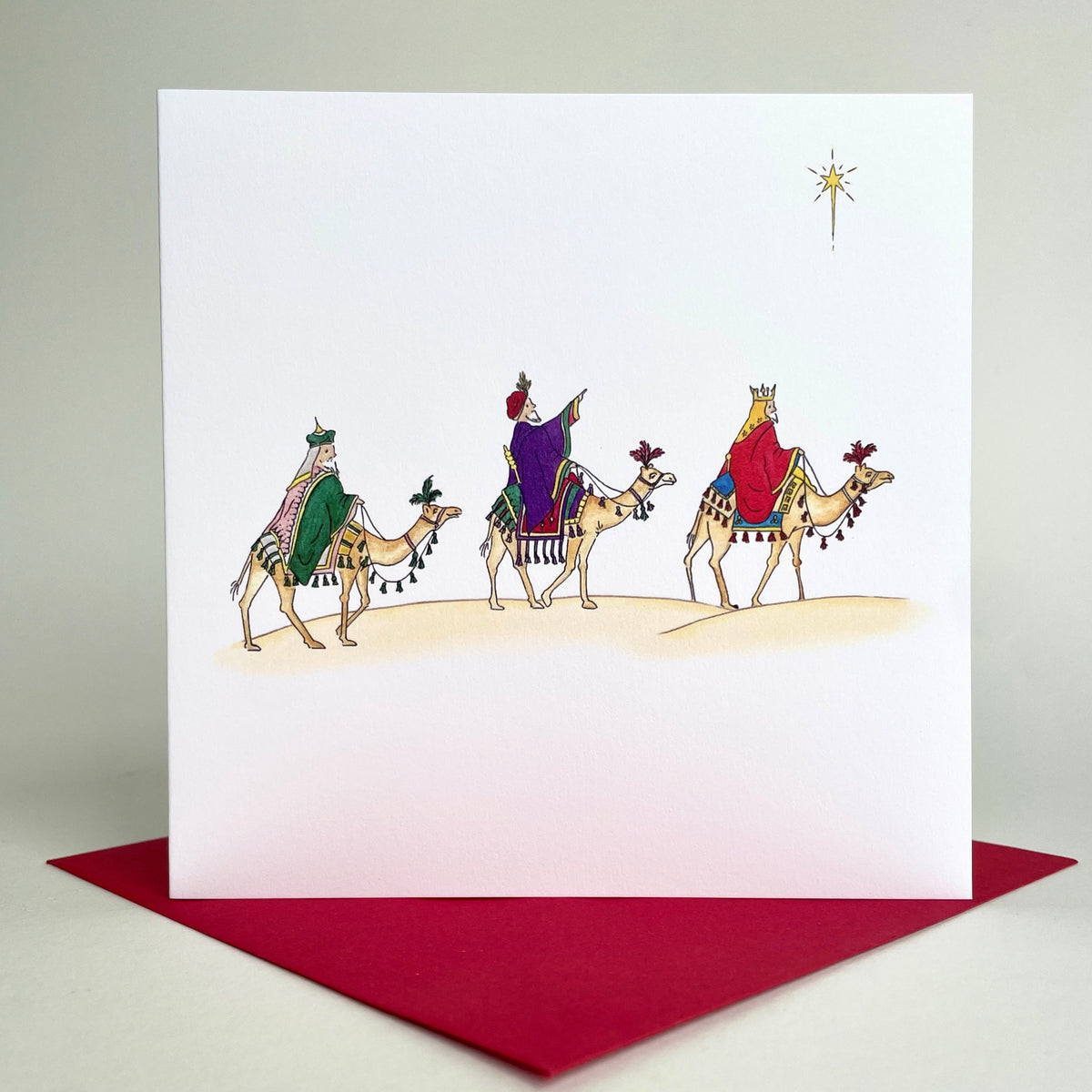 Square charity card with traditional Christmas illustration of the three wise men on camels following the star, set on coordinating crimson red envelope